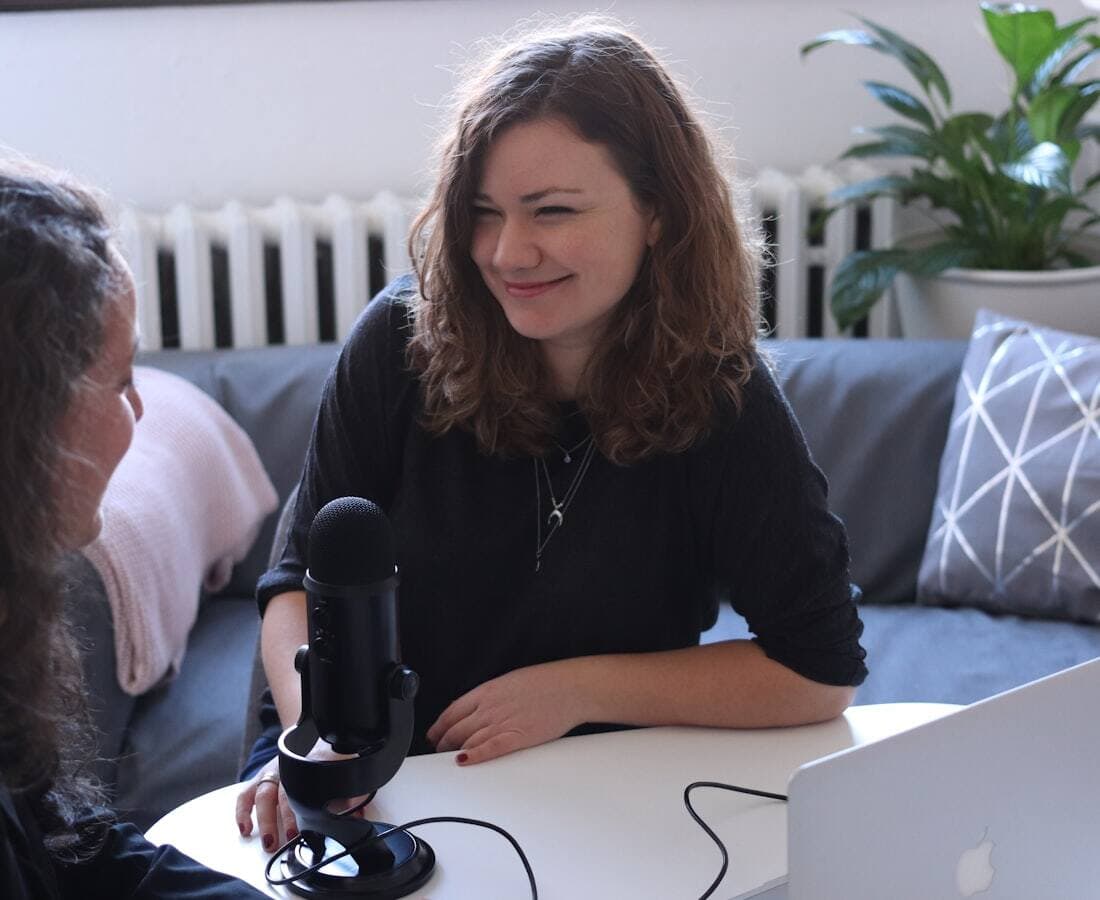 Two people recording a podcast conversation across a table of microphones