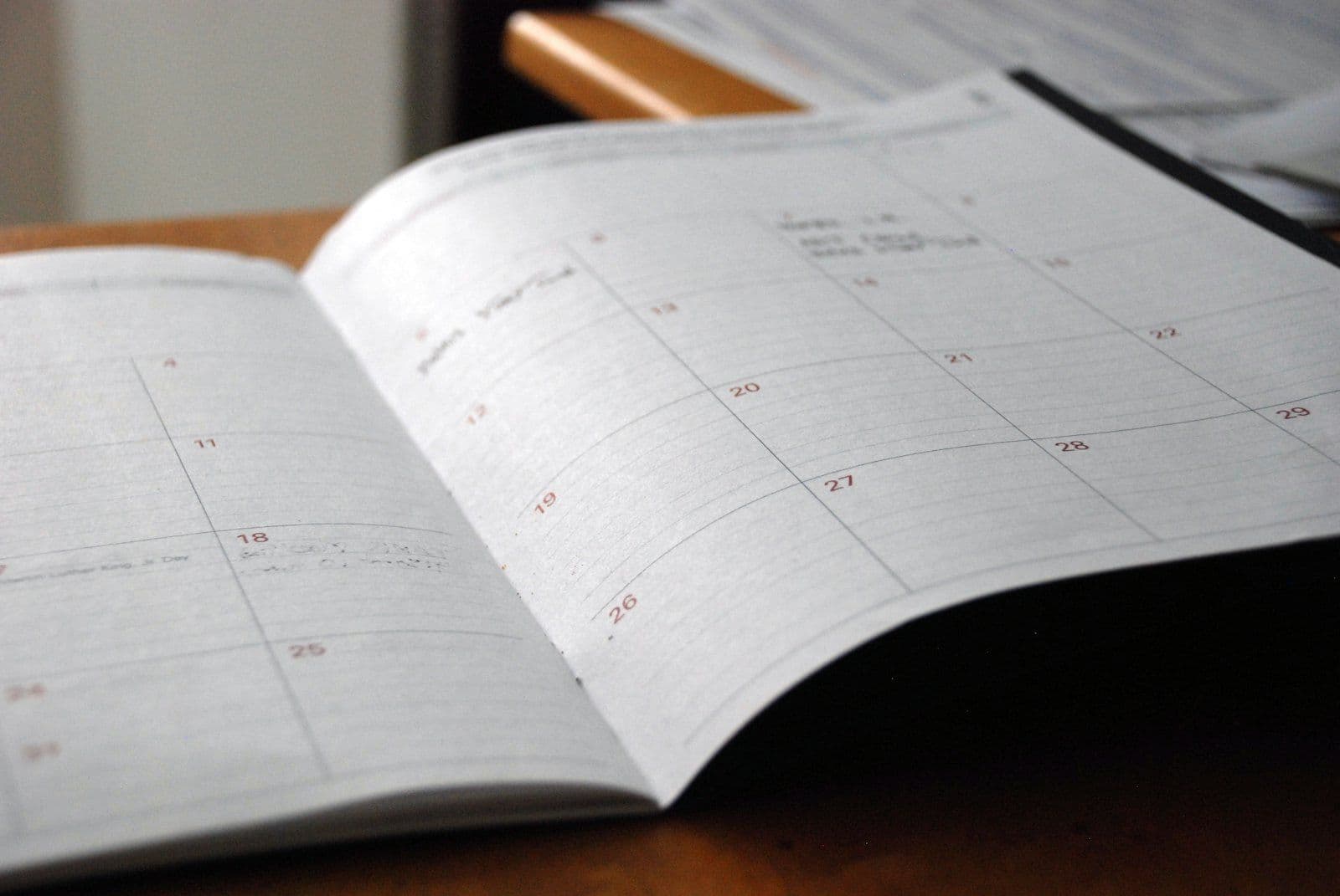 An open monthly planner lying on a wooden desk with the month's squares still empty