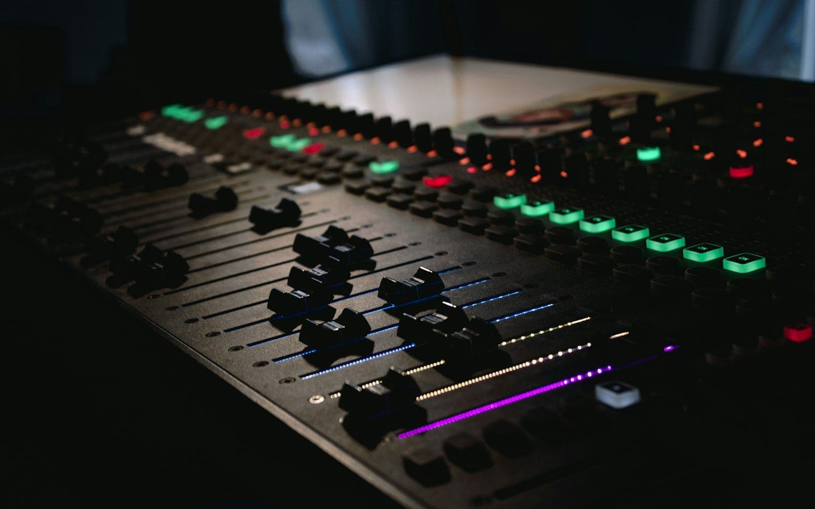 A studio audio mixing desk photographed close up, faders and knobs lit in green