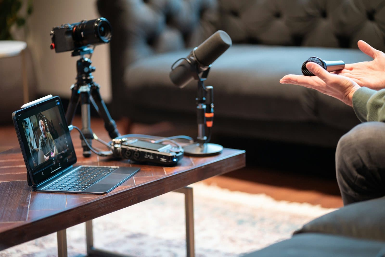 A podcast recording setup on a desk: a microphone on a stand beside an open laptop and a camera