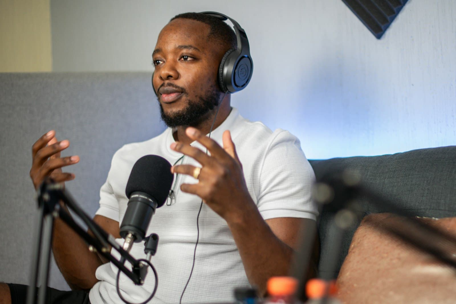 A podcast guest wearing headphones gestures while speaking into a broadcast microphone mid-interview