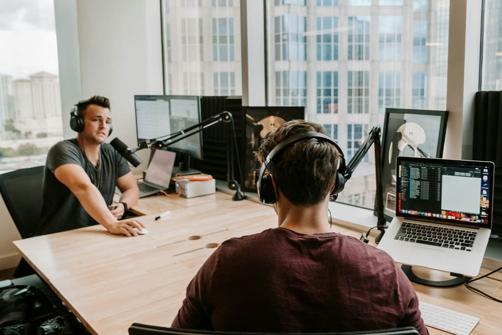 A podcast host at a studio microphone talks across the desk to a guest in headphones