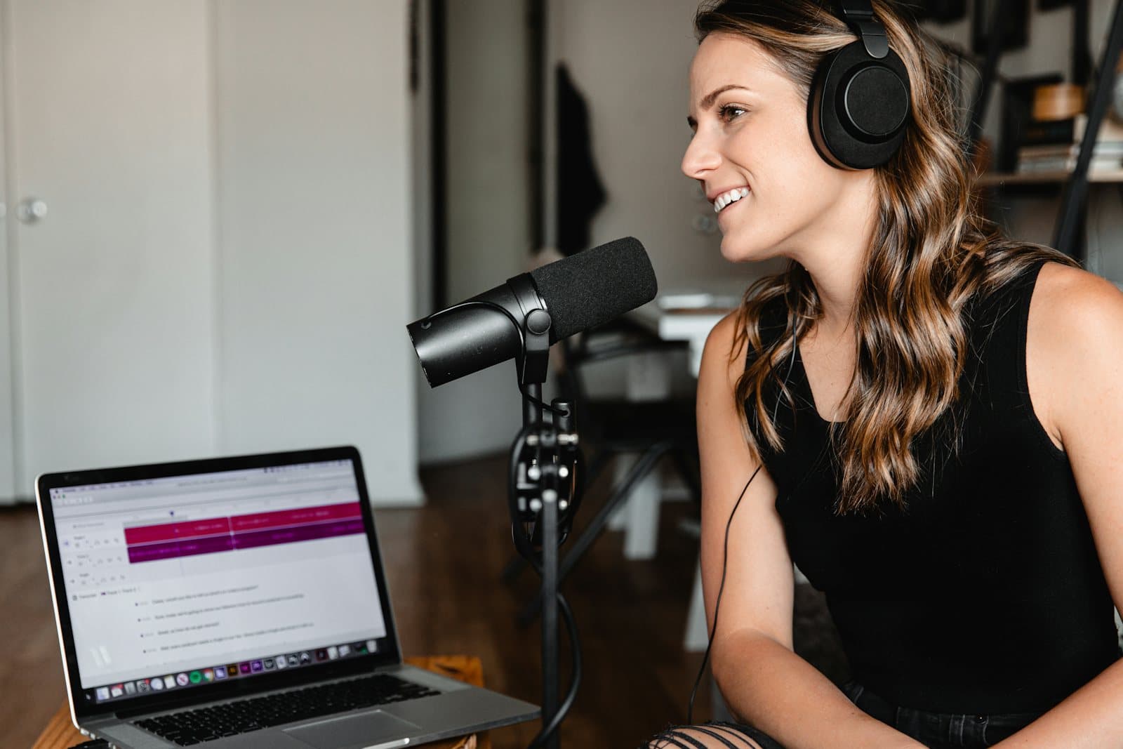 A guest with headphones reviews notes on a laptop while set up at a podcast microphone