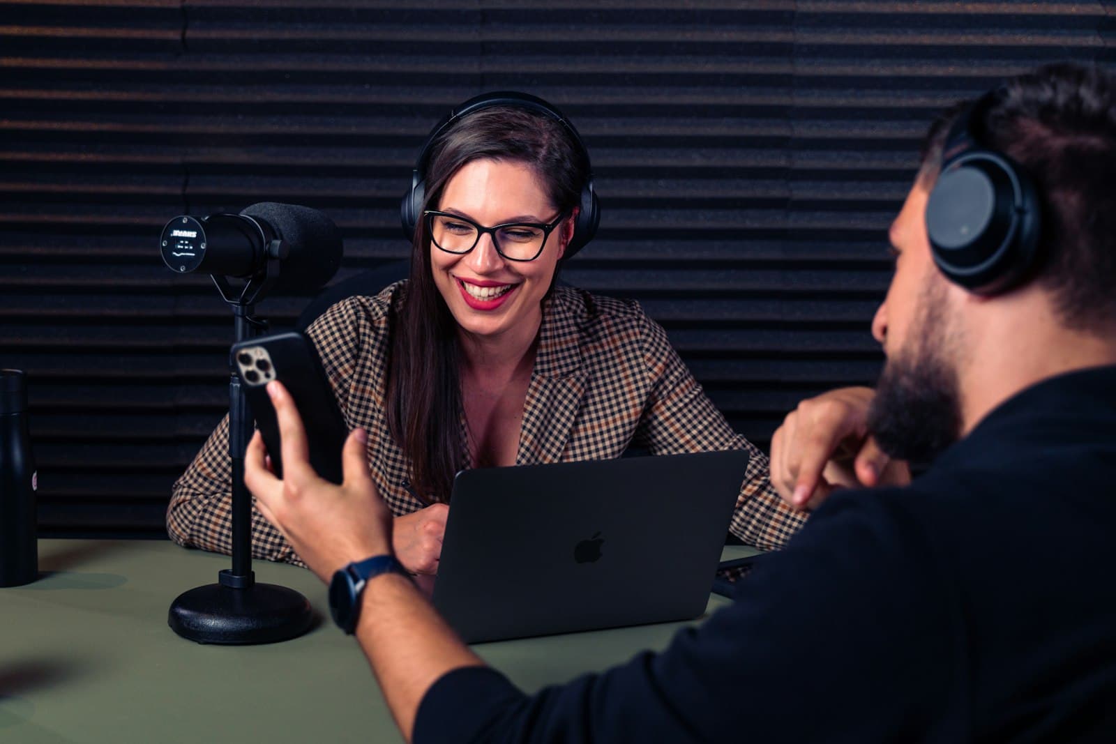 A podcaster films a short promo clip on a phone while recording with a guest in the studio