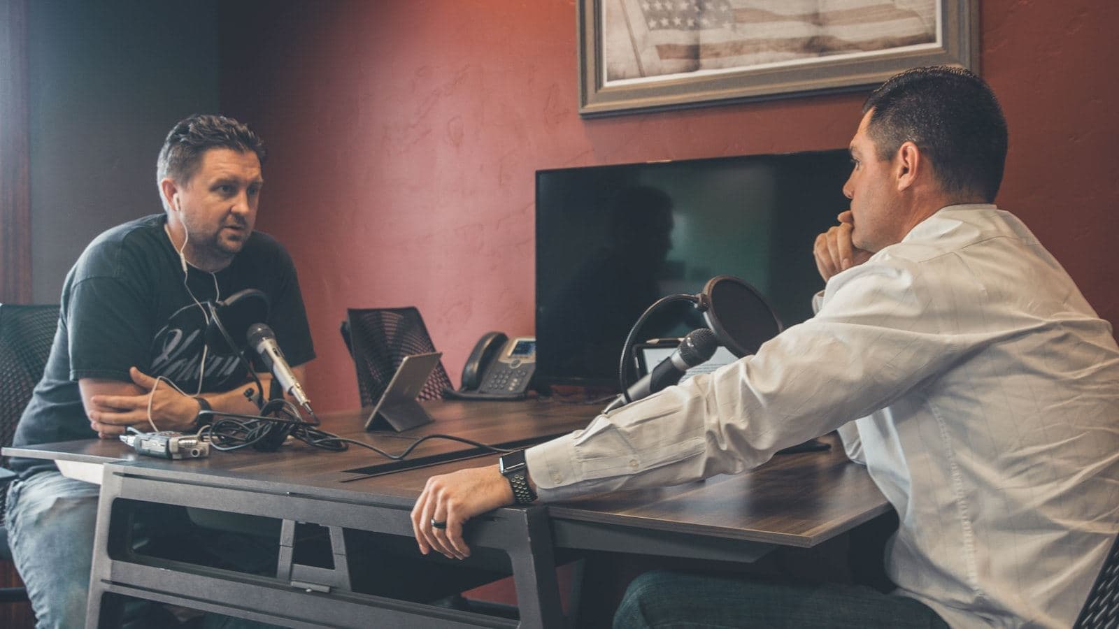 Two people seated across from each other mid-conversation in a recording room
