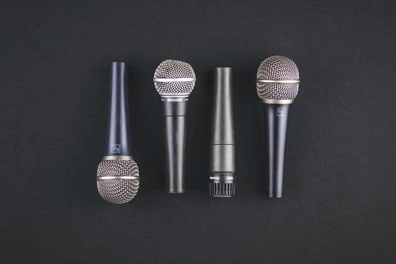 Four broadcast microphones lined up side by side on a table