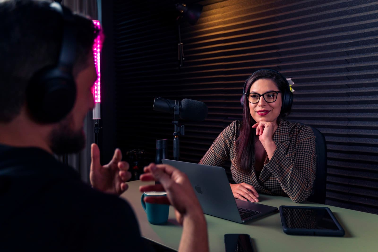 A host and guest share a laugh mid-conversation in a dimly lit podcast studio