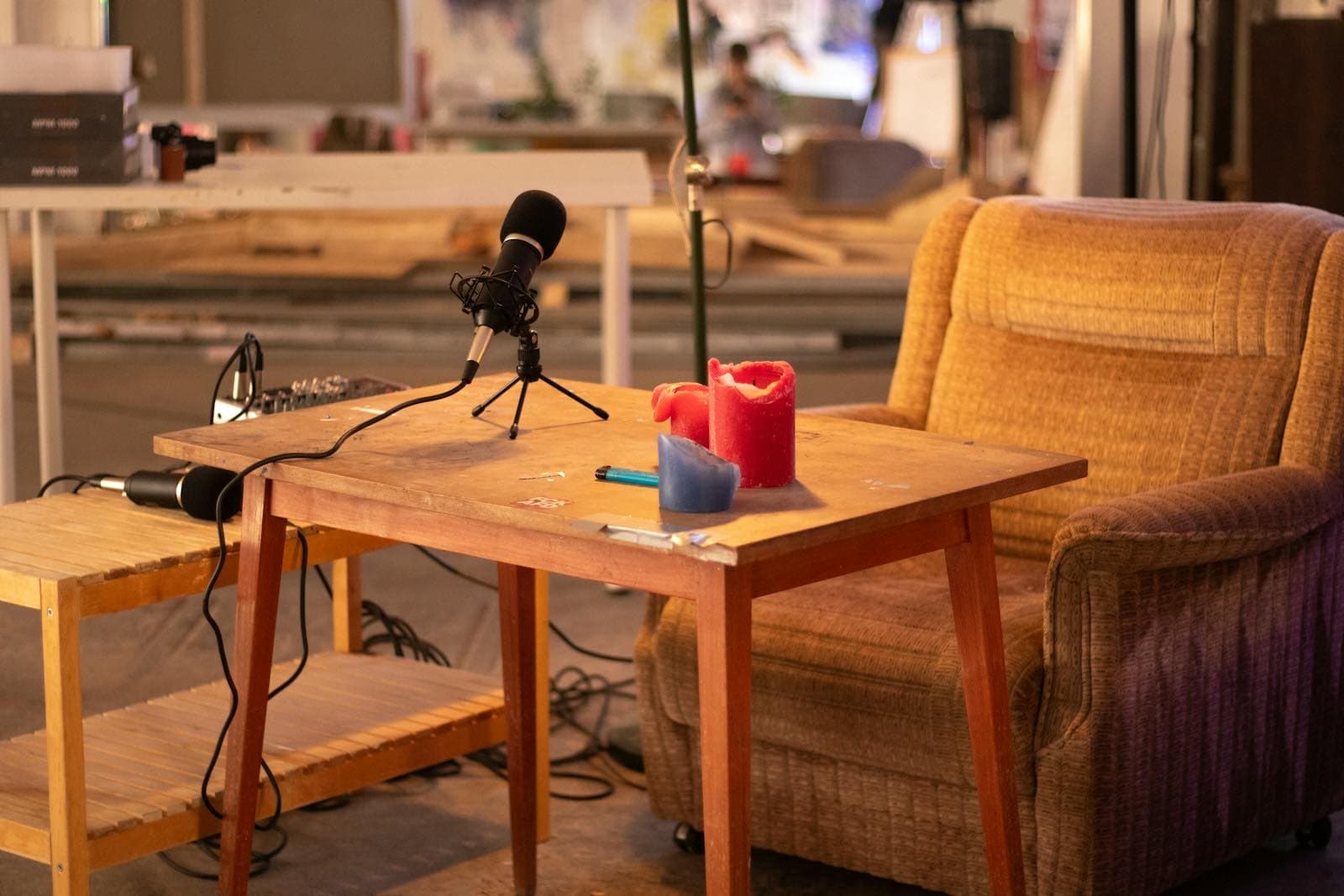 An empty armchair beside a microphone on a stand, lit by candles in a quiet room