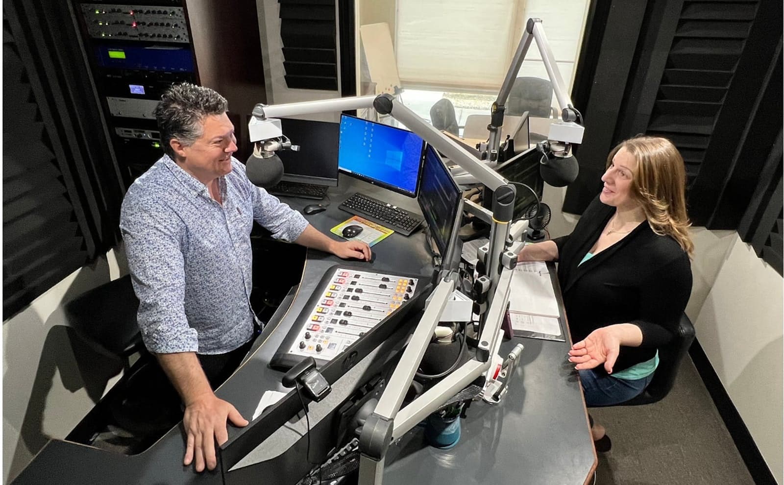 Two presenters talking across a mixing desk in a professional radio studio