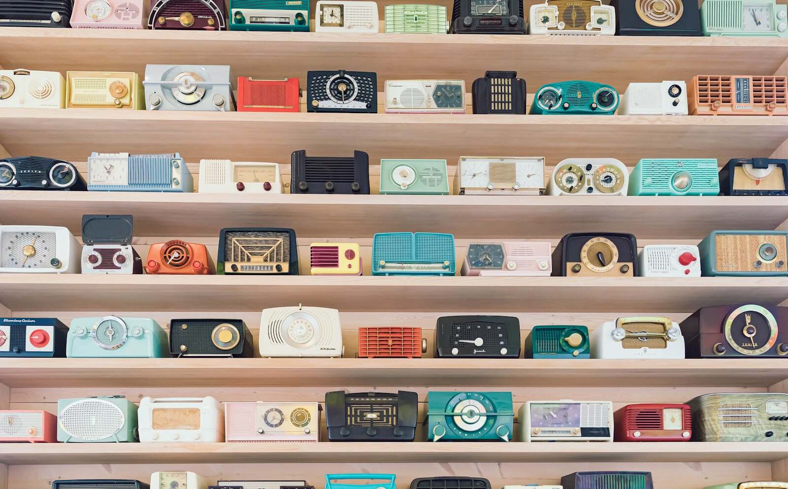A shelf packed with dozens of vintage radios of every size, side by side