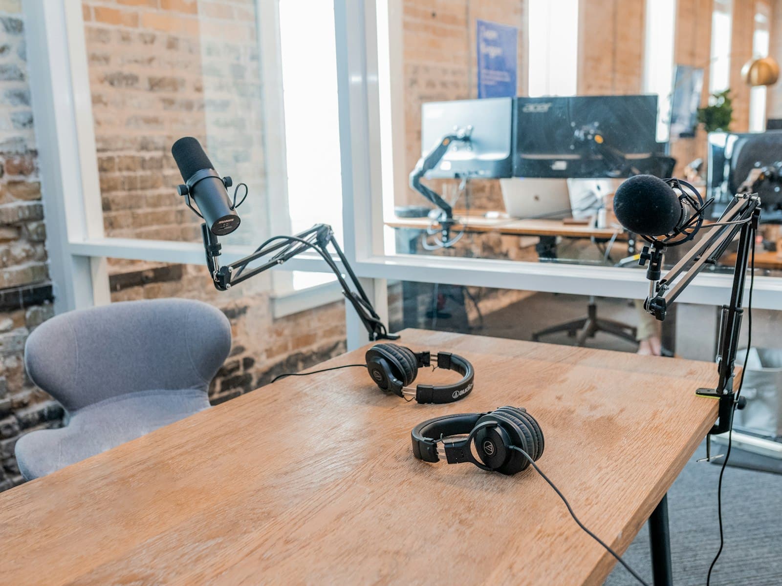 An empty guest chair at a wooden studio table with two microphones on boom arms and two pairs of headphones