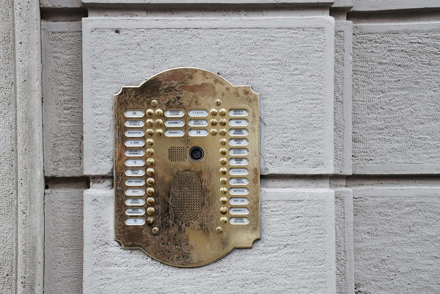 A weathered brass apartment intercom panel with rows of unlabelled buttons