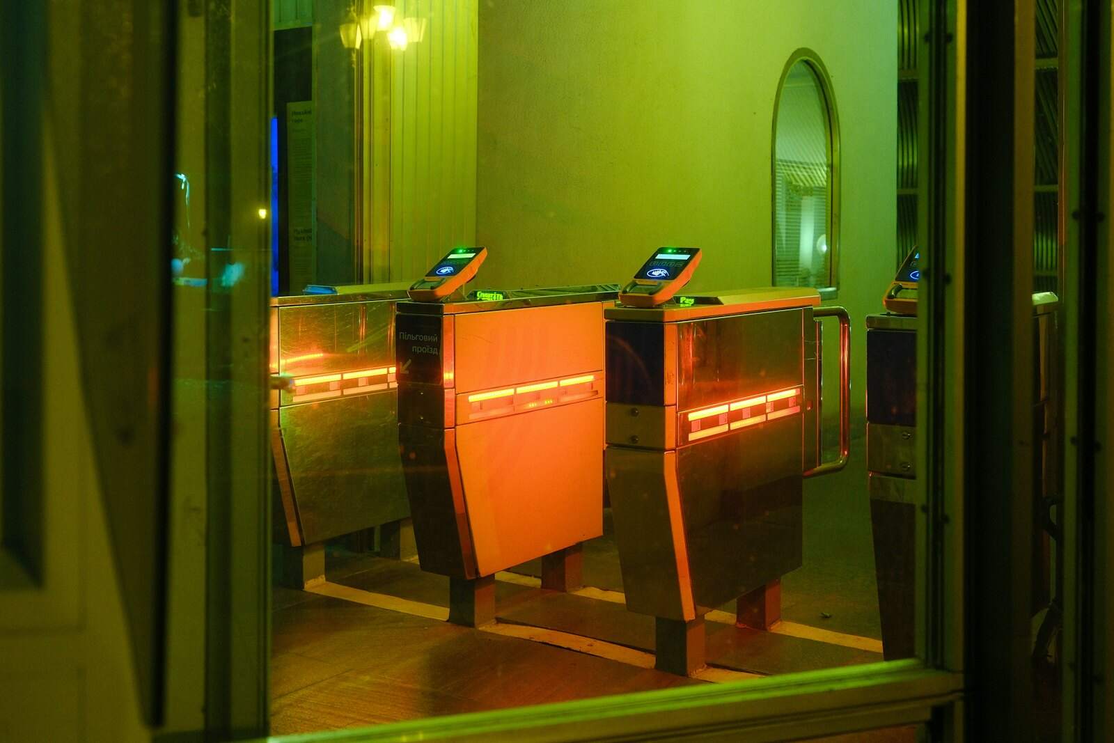 A row of ticket-gate turnstiles in a station entrance, lit in orange and green
