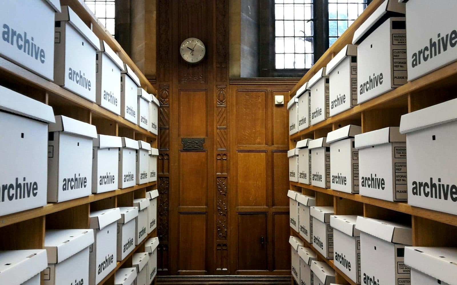 Rows of identical white archive boxes filling wooden shelves, receding out of frame