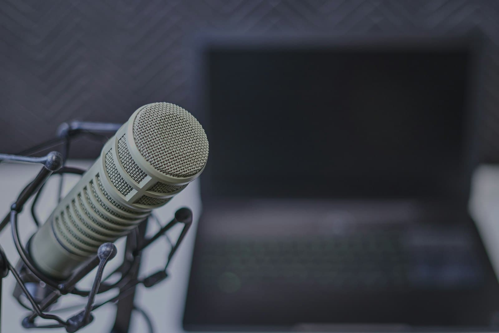 A condenser microphone on a stand beside an open laptop on a plain desk