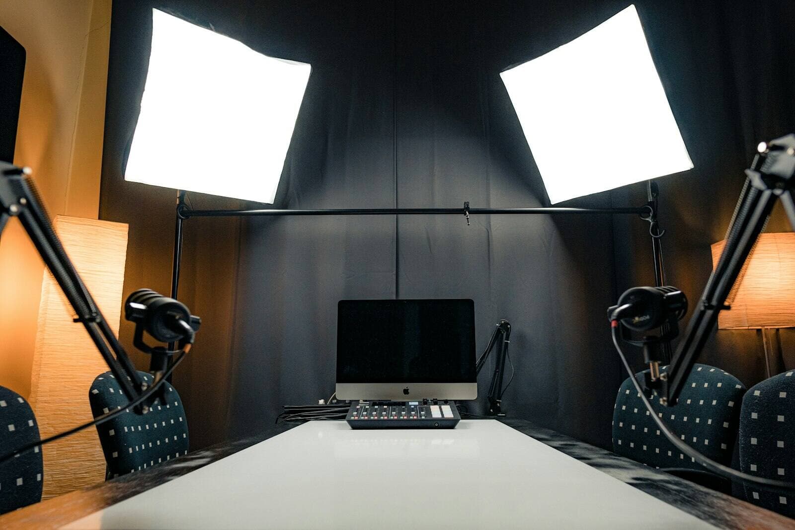 An empty podcast studio with a boom microphone on each side of a long table under two softbox lights