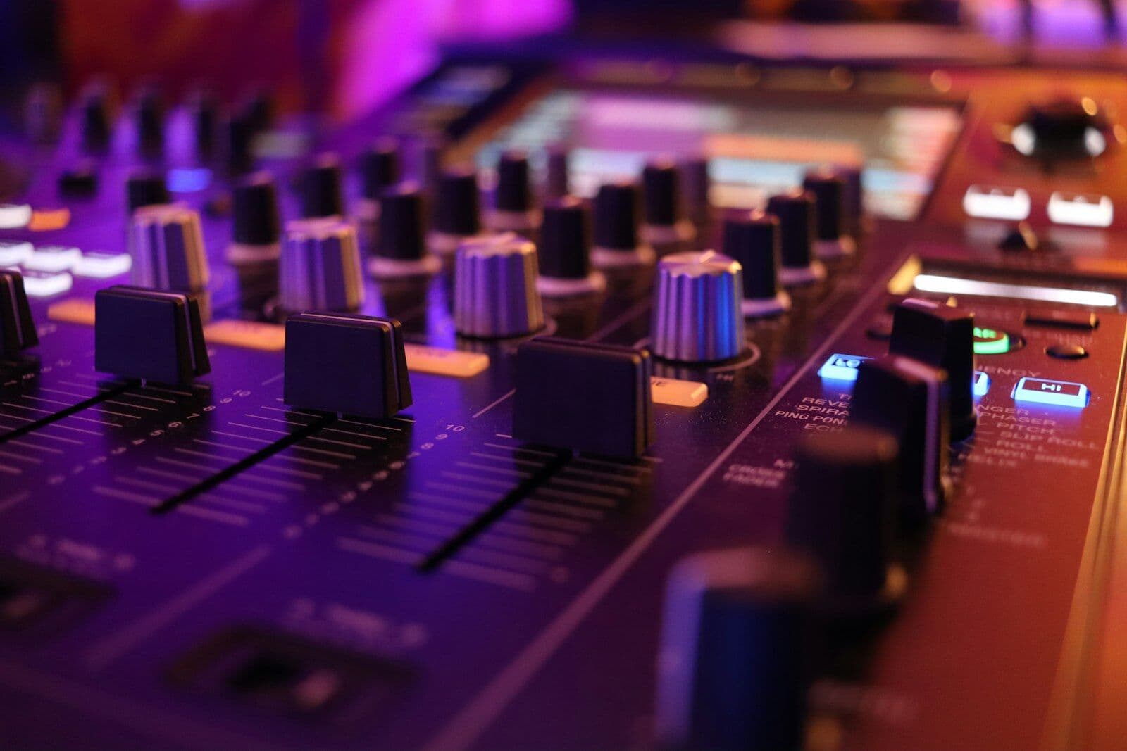 A close-up of a recording studio mixing board with rows of faders and dials