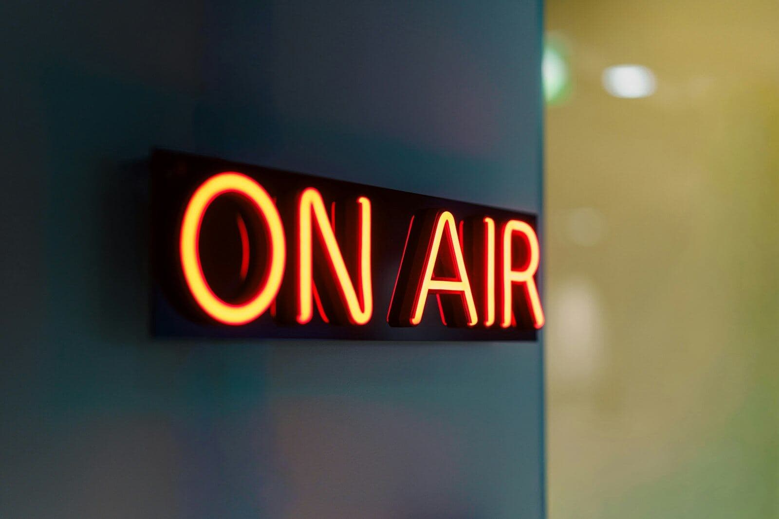 A red neon ON AIR sign glowing on a dark studio wall