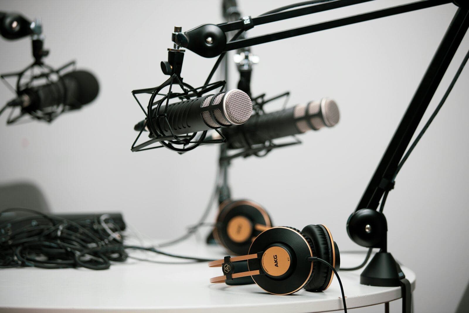 Three podcast microphones on boom arms above a white table, with two pairs of headphones resting on it