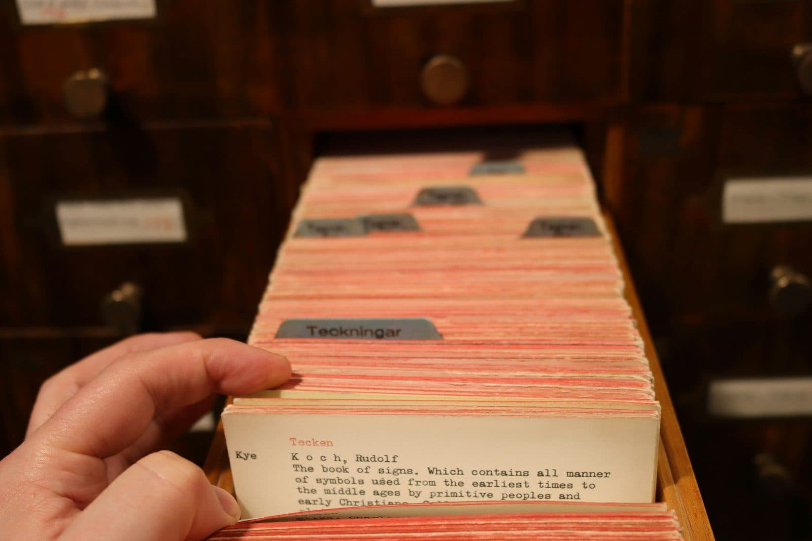A hand pulling a record card out of an open wooden library catalogue drawer
